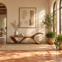 Bench with a flat plank seat, a swooping base and an upswept tail in a bright entryway with arched windows and plants