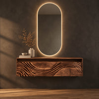 Floating makeup vanity with an open top niche and a wave carved front in a dark studio against a charcoal plaster wall