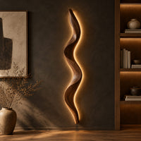 Tall wavy wall sconce that glows softly along its back edge in a dark studio against a charcoal plaster wall