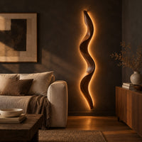Tall wavy wall sconce that glows softly along its back edge in a dark living room at golden hour