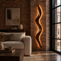 Tall wavy wall sconce that glows softly along its back edge in an industrial loft living room with exposed brick