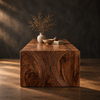 Waterfall dining table with carved swirl grain end panels in a dark studio against a charcoal plaster wall