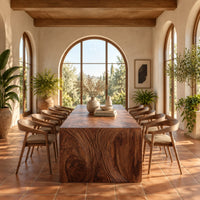 Waterfall dining table with carved swirl grain end panels in a bright dining room with arched windows and plants