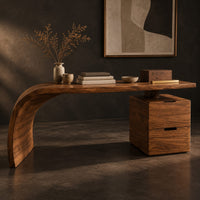 Corner detail of desk with a sweeping waterfall leg and a two drawer pedestal beside wood, brass and linen samples