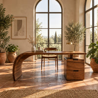 Desk with a sweeping waterfall leg and a two drawer pedestal in a bright home office with arched windows and plants