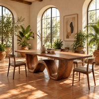 Rectangular dining table on a thick wave shaped base in a bright dining room with arched windows and plants
