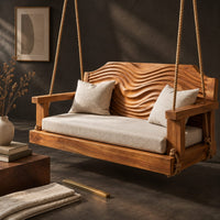 Corner detail of wooden swing with a wave carved back and a long seat cushion beside wood, brass and linen samples