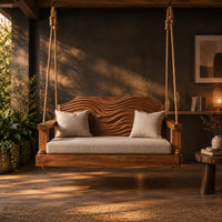 Wooden swing with a wave carved back and a long seat cushion in a dark porch at golden hour