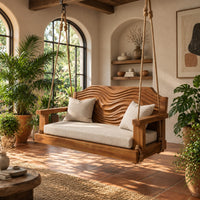 Wooden swing with a wave carved back and a long seat cushion in a bright porch with arched windows and plants