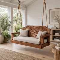 Wooden swing with a wave carved back and a long seat cushion in a Scandinavian porch with white walls