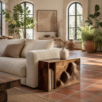 End table with a carved wave front and an open side compartment in a bright living room with arched windows and plants