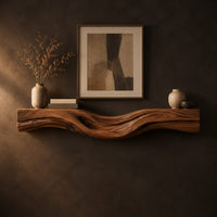 Thick wood fireplace mantel with a wave carved front and flowing grain in a dark studio against a charcoal plaster wall