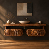Floating vanity with a thick slab top over two wave carved pods in a dark studio against a charcoal plaster wall