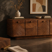 Corner detail of wooden sideboard with four wave carved doors and a plinth base beside wood, brass and linen samples