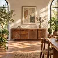 Wooden sideboard with four wave carved doors and a plinth base in a bright dining room with arched windows and plants