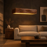 Linear wooden pendant light with wave carved sides and a glowing underside in a dark living room at golden hour