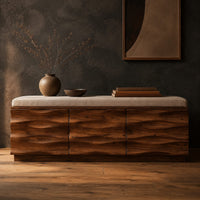 Bench with a padded seat and three wave carved front panels in a dark studio against a charcoal plaster wall