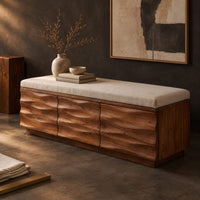 Corner detail of bench with a padded seat and three wave carved front panels beside wood, brass and linen samples