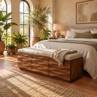 Bench with a padded seat and three wave carved front panels in a bright bedroom with arched windows and plants