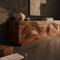 Corner detail of long sideboard with deep wave carving across the full front beside wood, brass and linen samples