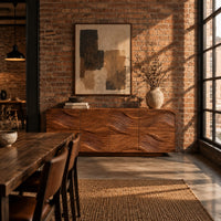 Wave carved wooden sideboard with four relief panels on a plinth base in an industrial loft dining room with exposed brick