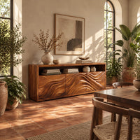Low sideboard with three carved wave panels and an open display shelf above in a bright dining room with arched windows and plants
