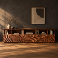 Low tv stand with wave carved front panels and a row of open cubbies in a dark studio against a charcoal plaster wall