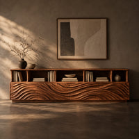 Corner detail of low tv stand with wave carved front panels and a row of open cubbies beside wood, brass and linen samples