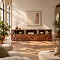 Low tv stand with wave carved front panels and a row of open cubbies in a bright living room with arched windows and plants