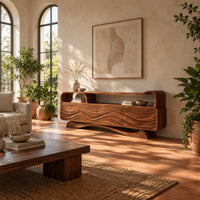 Tv stand with wave carved panels, an open top shelf and an arched base in a bright living room with arched windows and plants