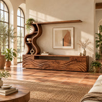 Long wood media cabinet with wave carved fronts and an s shaped shelf tower in a bright living room with arched windows and plants