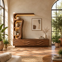 Low wave carved cabinet with a tall open shelf tower and a top shelf in a bright living room with arched windows and plants