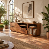 Low wooden tv stand with a wave cut front and upright slots in a bright living room with arched windows and plants