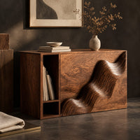 Corner detail of boxy side table with a carved wave front and an open book slot beside wood, brass and linen samples
