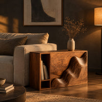 Boxy side table with a carved wave front and an open book slot in a dark living room at golden hour