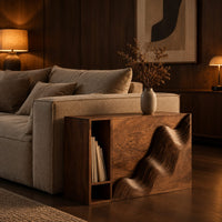 Boxy side table with a carved wave front and an open book slot in an evening living room with walnut wall paneling