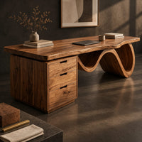 Corner detail of desk with a thick slab top, three drawer pedestal and a wave shaped leg beside wood, brass and linen samples