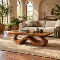 Rectangle coffee table with softly shaped corners on a flowing wave loop base in a bright living room with arched windows and plants