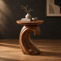 Side table with a wave shaped pedestal and a circular top in a dark studio against a charcoal plaster wall
