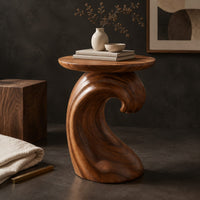 Corner detail of side table with a wave shaped pedestal and a circular top beside wood, brass and linen samples