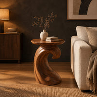 Side table with a wave shaped pedestal and a circular top in a dark living room at golden hour