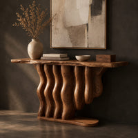Corner detail of console table with a base of wavy wood columns on an oval foot beside wood, brass and linen samples