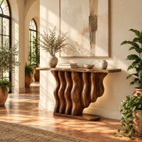 Console table with a base of wavy wood columns on an oval foot in a bright entryway with arched windows and plants