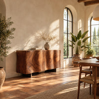 Wavy edged sideboard with two front panels and bold wood grain in a bright dining room with arched windows and plants