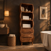 Tall bathroom cabinet with three wavy open shelves and three drawers in a dark bathroom at golden hour