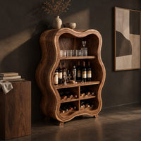Corner detail of tall wavy outline bar cabinet with open shelves and four wine cubbies beside wood, brass and linen samples
