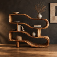 Wavy ribbon bookshelf with open shelves joined by chunky square posts in a dark studio against a charcoal plaster wall