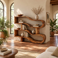 Wavy ribbon bookshelf with open shelves joined by chunky square posts in a bright living room with arched windows and plants