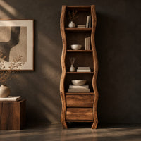 Corner detail of tall narrow cabinet with wavy sides, four open shelves and two drawer fronts below beside wood, brass and linen samples