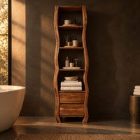 Tall narrow cabinet with wavy sides, four open shelves and two drawer fronts below in a dark bathroom at golden hour